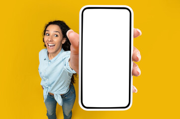 Check This Great App. Emotional Woman Holding Big White Empty Smartphone Screen In Hand Showing Cellphone Display Close Up To Camera, Recommending App On Orange Studio Wall. Above High Angle Top View