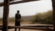 © inamii - Man in traditional clothing gazes thoughtfully across arid landscape framed by rustic wooden structure, evoking contemplation and resilience in harsh environments.