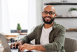 © Prostock-studio - Portrait of happy mature latin man sitting at desk, working on pc laptop and smiling at camera, free space. Excited male freelancer enjoying distant job, internet and modern technology