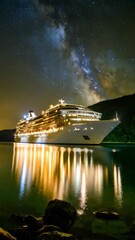 Wall Mural - Illuminated cruise ship reflects on calm ocean at night with Milky Way in background showing starry sky for tranquil nautical vacation theme