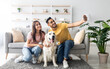 © Prostock-studio - Happy interracial couple taking selfie with their dog while sitting on soft carpet at home, full length. Positive Arab guy and his girlfriend making photo with cute pet in living room