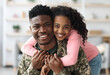 © Prostock-studio - Portrait of cheerful pretty curly black teen girl hugging her dad soldier from behind and smiling at camera, young black man in military uniform return home from army, cuddling with his daughter