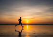 © ABIR HASAN - Silhouette of a lone person running on a wet sandy beach at sunset with vibrant orange and purple sky reflecting on the water