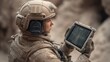 © 69 - Female soldier using portable tablet device outdoors in military environment for communication and tactical operations in sandy terrain