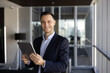 © fizkes - Portrait of businessman holds digital tablet in office hallway
