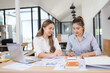 © SOMKID - Two businesswomen discussing work using digital tablet and laptop in modern office, Business team analyzing financial data on a digital tablet and paper report.