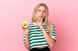 © luismolinero - Young caucasian woman holding an avocado isolated on pink background having doubts