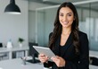 © Ozz - Smiling businesswoman holding a tablet in a modern office setting.