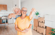 © luciano - Cheerful senior couple hug moving into a new home, surrounded by moving boxes in an empty room. The woman holding house keys, excited for their new beginning, real estate, property concept