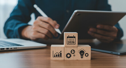 Person using tablet and stylus with technology icons on wooden block and laptop