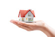 © Gio - Hand Holding a Small White House Model with Red Roof Against a Black Background
