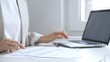 © rogerphoto - Professional female analyzing financial reports, reviewing charts on laptop and paper documents while seating at the desk in office. Business people