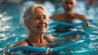 © Johannes - smiling senior woman doing aqua fitness with swim noodles happy mature healthy woman taking fitness classes in aqua aerobics healthy old woman holding swim noodles doing aqua gym with young trainer n