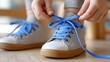 © Belvedere studio - Child ties blue shoelaces on grey sneakers while sitting indoors in a cozy environment, capturing a moment of learning and independence