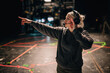© Olena - A blonde female production assistant, stage manager with headphones points on a dark stage. Woman directs during a show's filming with various technical markings on the floor. Live event production.