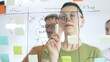 © volha_r - Professional team brainstorming, sharing strategy on glass whiteboard with colorful sticky notes, working collaboratively in bright office space. Business people concept