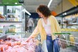 © Serhii - Woman choosing cold cuts in supermarket refrigerated display case