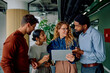 © we.bond.creations - Four business colleagues collaborating on a new project standing in a modern office, analyzing data on a digital tablet