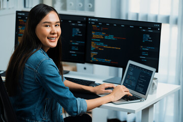 Young Asian in IT developer looking at camera to present with online information on pc with coding program data application, wearing jeans shirt. surround by safety analysis two screens. Stratagem.