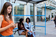 © Oscar - Young woman using smartphone at bus stop while waiting for public transport