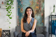© Studio Marmellata - A young woman with dark curly hair smiles while sitting in a modern studio with plants and artwork.
