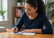 © Kinza - Focused woman diligently writing notes in a bright home office, planning her next steps for success.