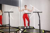 Smiling woman showing her biceps on mini exercise trampoline in fitness studio, low angle view