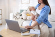© New Africa - Telehealth. Mother with her baby having online consultation with doctor on sofa indoors, closeup