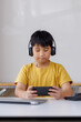 © Phimwilai - Young student wearing headphones playing mobile game at home