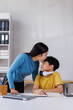 © Phimwilai - Asian mother kissing son doing homework at home office desk