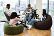 © sofiko14 - Diverse group of professionals collaborating in modern office environment focusing on teamwork. Young individuals from different backgrounds, including man in wheelchair, seated around bean bags.