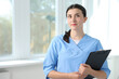 © New Africa - Nurse with clipboard near window in clinic, space for text