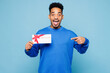 © ViDi Studio - Young man of African American ethnicity wears sweatshirt casual clothes hold point on gift certificate coupon voucher card for store isolated on plain pastel blue cyan background. Lifestyle concept.