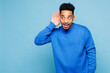 © ViDi Studio - Young curious nosy man of African American ethnicity wear sweatshirt casual clothes try to hear you overhear listening intently isolated on plain pastel light blue cyan background. Lifestyle concept.