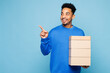 © ViDi Studio - Young man of African American ethnicity wear sweatshirt casual clothes hold stack cardboard blank boxes point finger aside isolated on plain pastel light blue cyan background studio Lifestyle concept