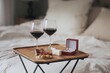 © The 2R Artificiality - A portable table set on a mattress with a soft cover, featuring two glasses of red wine, assorted cheeses like blue cheese, camembert, and brie, cured ham, ciabatta bread, a romantic proposal setup