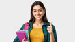 © Shivani - A young Indian student girl with long hair gives a thumbs up, holding colorful books and wearing a casual plaid shirt and backpack