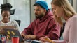 © Yuliia - Three concentrated informal business diversity people together team focused indoor in office Indian pensive man with laptop thinking Caucasian female writing notes African American woman with computer