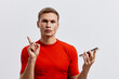 © SHOTPRIME STUDIO - Young caucasian man in red shirt hold smartphone point finger use voice assistant digital technology concept isolated white background studio portrait