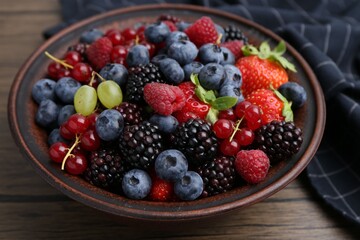 Wall Mural - Different ripe berries in bowl on wooden table, closeup