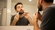© Felippe Lopes - A man trims his beard with an electric razor while looking in the mirror of a bright bathroom focused on personal grooming and hygiene