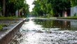 © James - A street floods during a downpour, with a sidewalk, curb, and trees blurred in the background under the rain