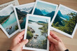 © AnnaStills - Caucasian young adult hands holding landscape photograph with four additional scenic mountain and lake photos spread on wooden surface, showcasing nature photography collection