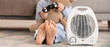 © Pixel-Shot - Electric fan heater and barefoot little girl playing video game on floor at home, closeup