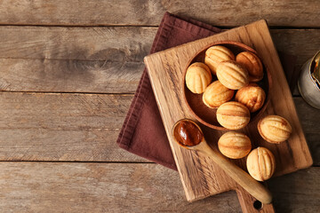 Wall Mural - Cutting board with tasty walnut shaped cookies and boiled condensed milk on wooden background