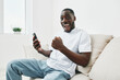 © SHOTPRIME STUDIO - Happy young man celebrating success while using his smartphone in a bright living room, showing excitement with casual attire