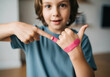 © smth.design - Smiling child showing pink adhesive bandages on finger and thumb indoors, demonstrating first aid treatment for minor injuries