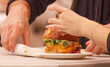 © arazu - Two people at a food festival in Karlín Square, Prague, sharing a freshly prepared gourmet burger with melted cheese and vegetables, highlighting a social dining moment.