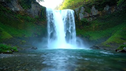 Wall Mural - ﻿Slow motion wide shot of a powerful waterfall cascading into a pristine, clear river, enveloped in soft morning light energy, water, remote