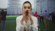 Young hispanic woman doctor wearing clear glasses raises hand with stethoscope at pisa tower building; concern.